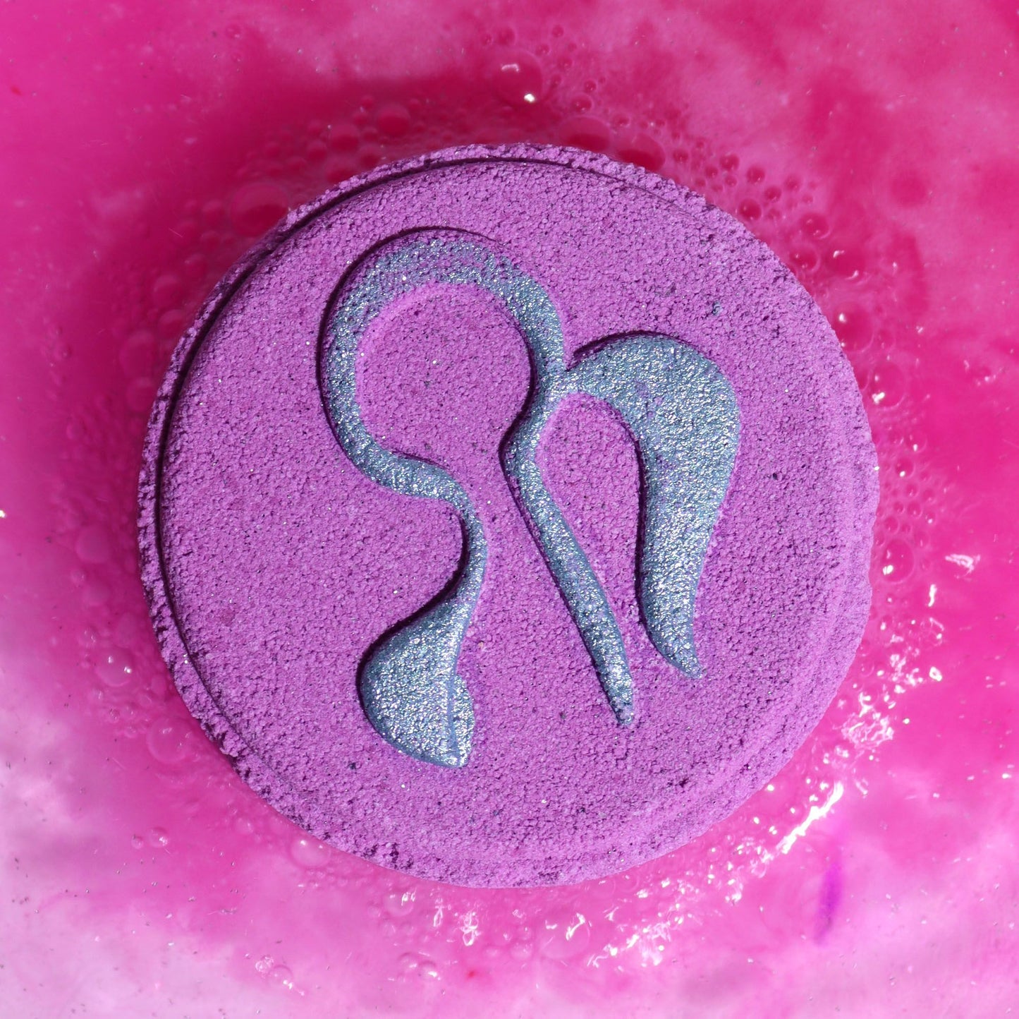 Purple bath bomb with a symbol on a pink bubble bath background