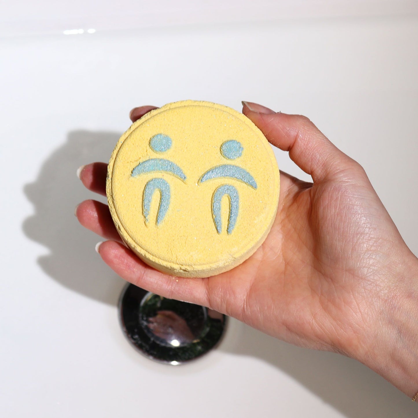 Hand holding a yellow bath bomb with blue symbols on a white background