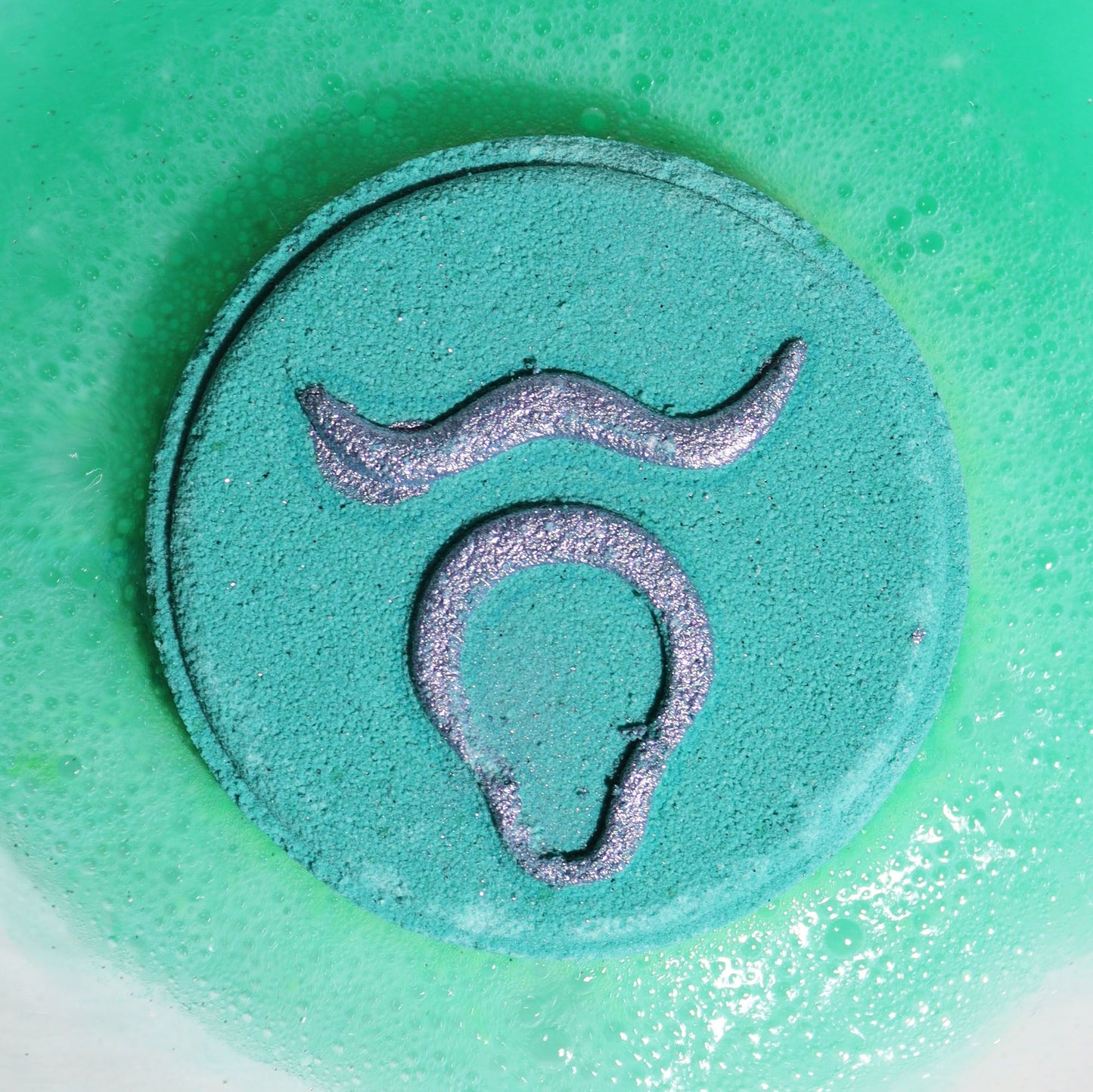 Circular bath bomb with a snake design on a green background